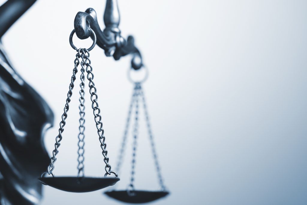 Close up detail of the scales of justice being held aloft by a small statue of Justice over a grey background with copy space conceptual of law and order